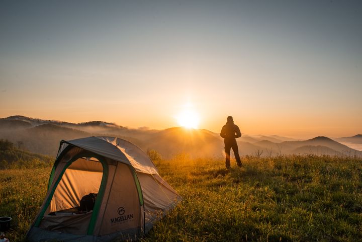 Hiker standing near camping tent on top of a mountain looking at sunset in Hong Kong 