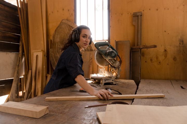 woman holding a wood plank in front of miter saw