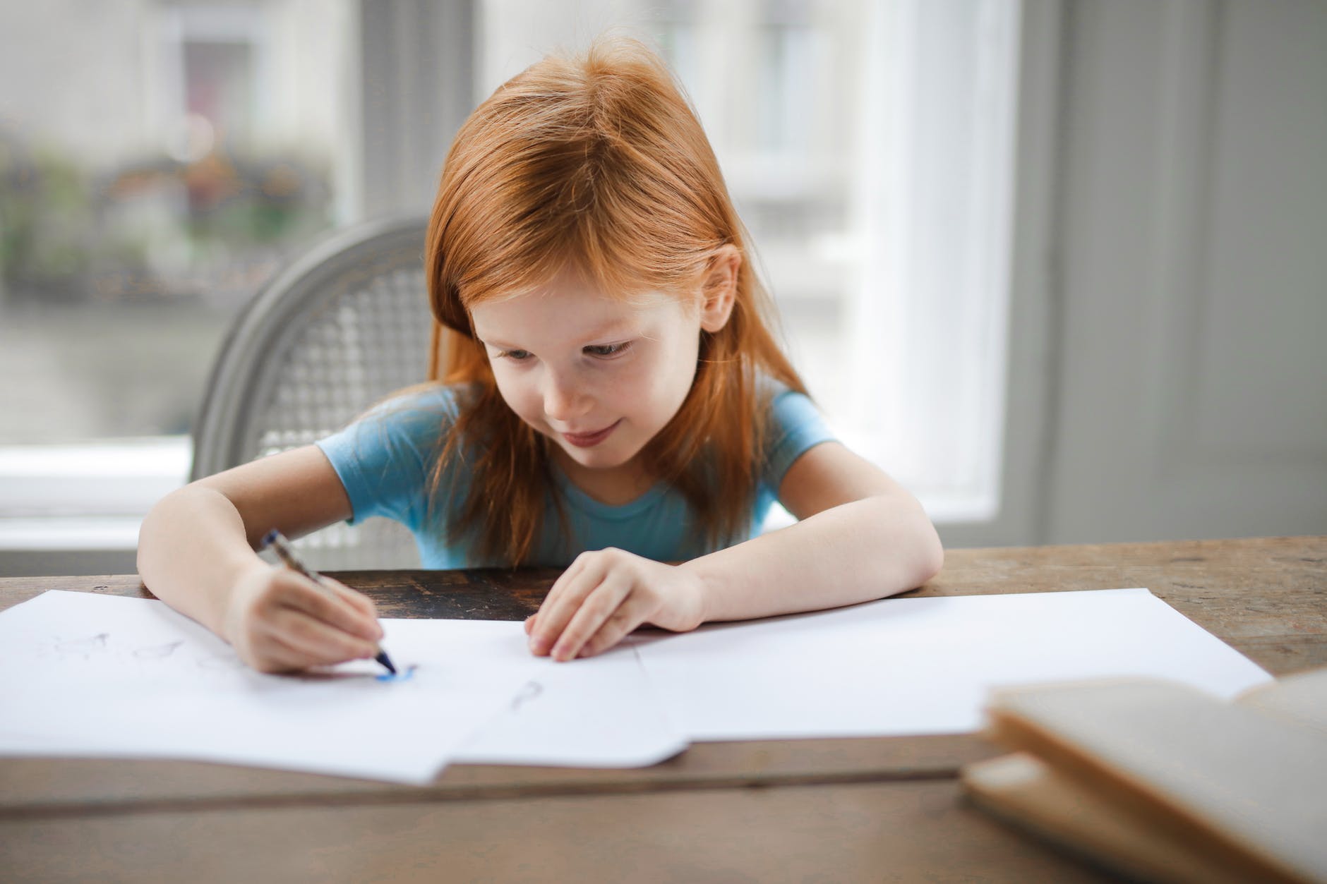 diligent small girl drawing on paper in light living room at home