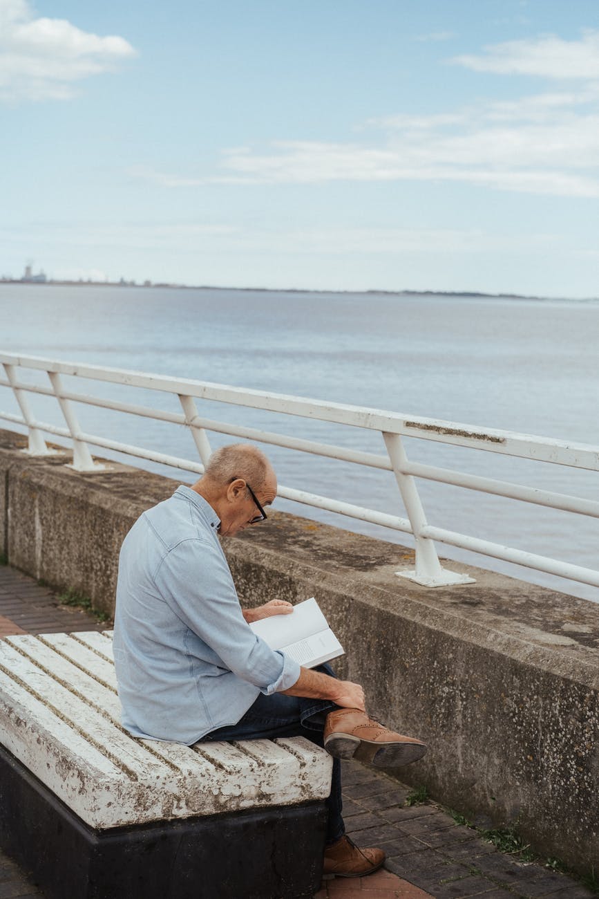elderly man reading book sitting on embankment