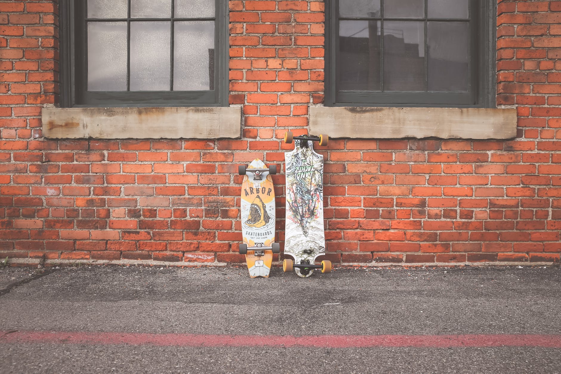 two white and brown longboard leaning on brown bricks wall